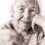 Sad elderly woman sitting at the table at home and looking miserably at only remaining coin from pension in her hand.
